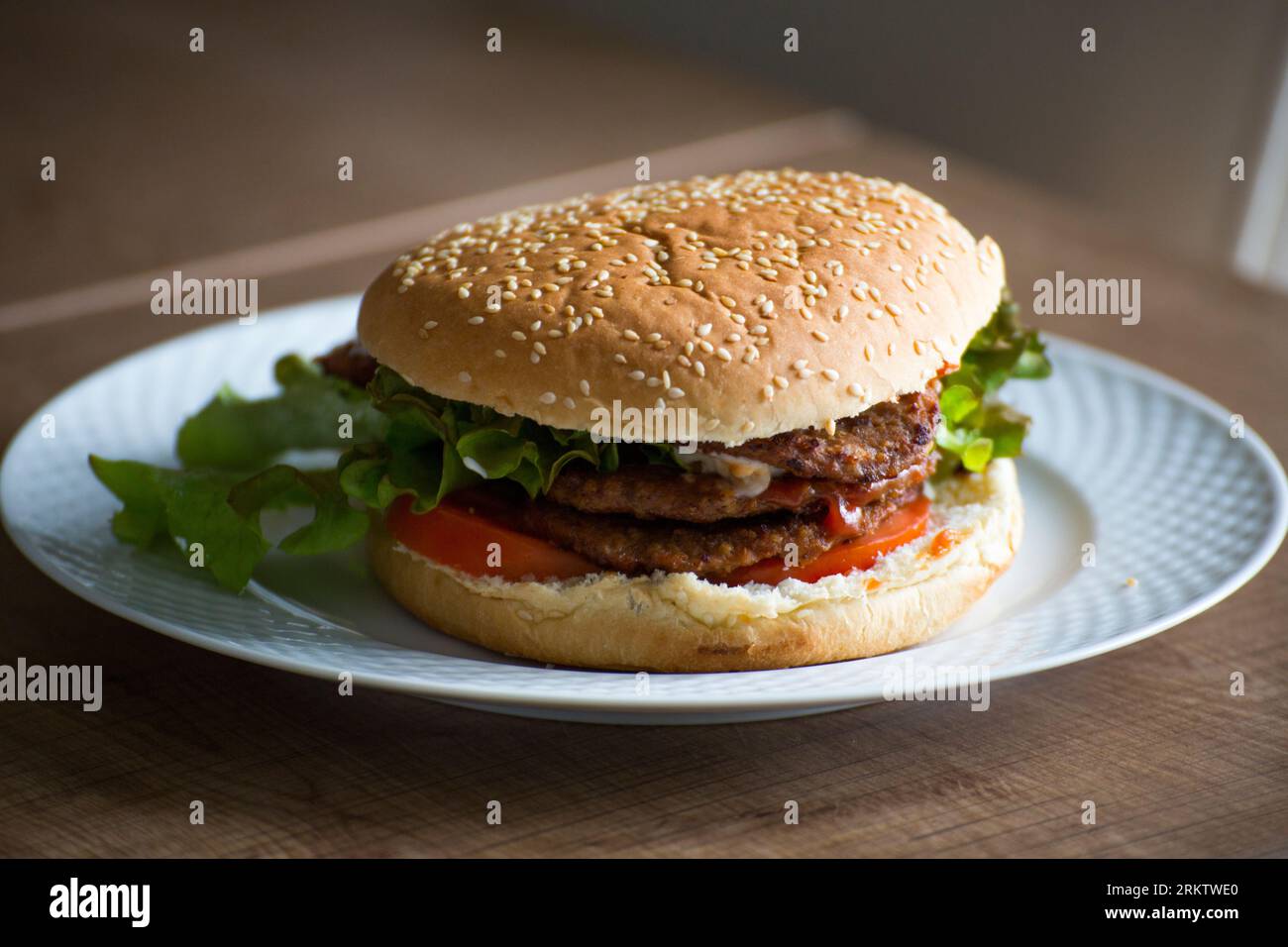 Doppio hamburger fatto in casa con lattuga e pomodoro in un piatto bianco sul tavolo da pranzo Foto Stock