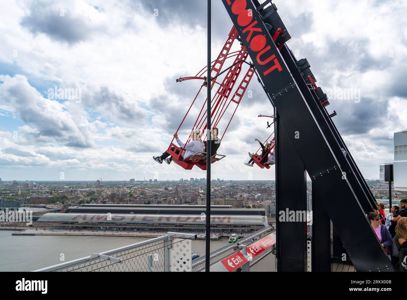 Amsterdam, Olanda - 17 luglio 2023: Persone con l'altalena rossa che oscillano in alto nello spazio aereo contro lo splendido cielo blu sopra la città. Foto Stock