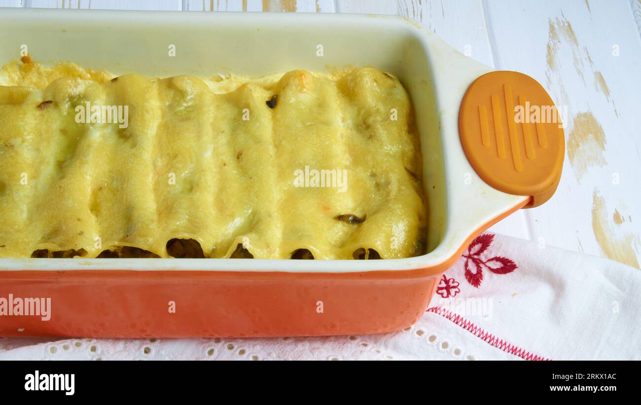 Cannelloni italiani con crema in ceramica arancio su tavola di legno bianco e tovaglia per primo piano fotografia di cibi per pubblicità, blog, mag Foto Stock