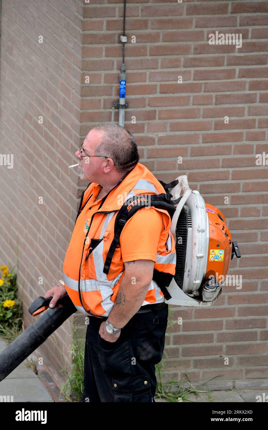 Lavoratore municipale con sigaretta in bocca che lavora con un soffiatore di foglie Foto Stock