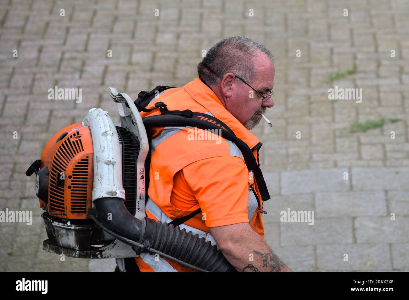 Lavoratore municipale con sigaretta in bocca che lavora con un soffiatore di foglie Foto Stock