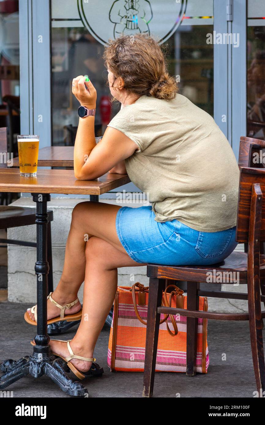 Donna in sovrappeso al tavolo da bar sulla terrazza con bicchiere di birra - Tours, Indre-et-Loire (37), Francia. Foto Stock