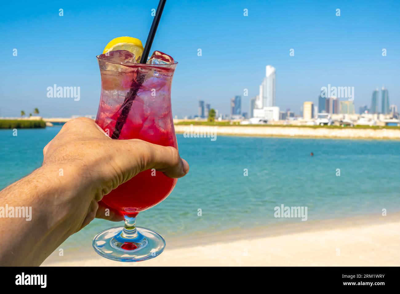 Bicchiere di bevanda rossa, limonata con limone e paglia contro Bahrain Bay, skyline del Medio Oriente Foto Stock