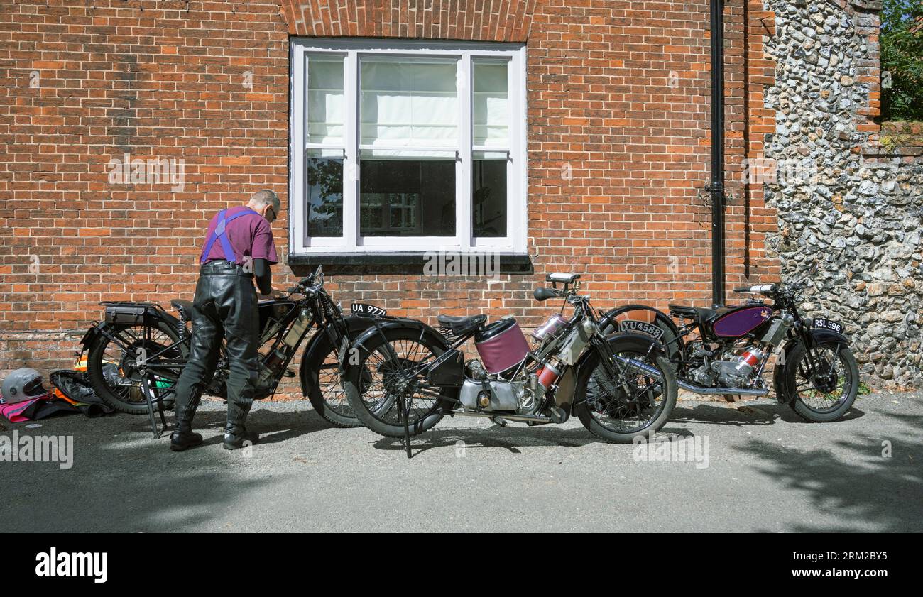 Un uomo più anziano con una maglia viola controlla la sua moto d'epoca in un raduno di motociclette a Castle acre, nel Norfolk, Inghilterra Foto Stock