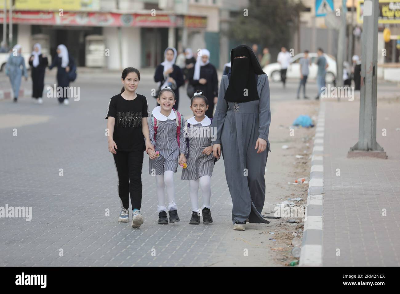 Una madre palestinese porta i suoi figli il primo giorno scolastico del nuovo anno nella loro scuola dell'Agenzia delle Nazioni Unite per il soccorso e l'occupazione dei rifugiati palestinesi (UNRWA) nella città di Gaza. Foto Stock