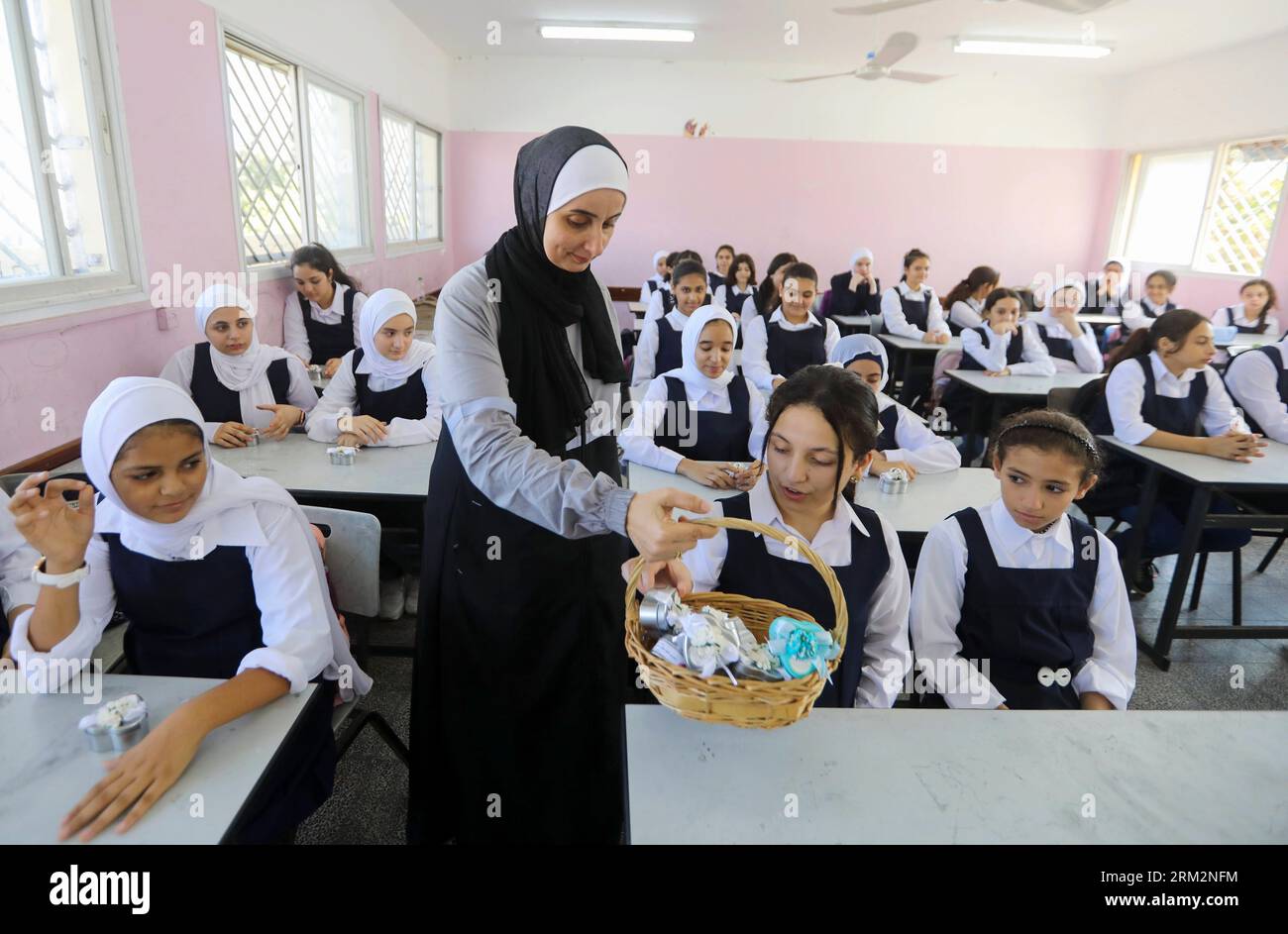 Un insegnante palestinese distribuisce dolci agli studenti il primo giorno scolastico del nuovo anno all'interno della loro scuola dell'Agenzia delle Nazioni Unite per il soccorso e l'occupazione dei rifugiati palestinesi (UNRWA) nella città di Gaza. Foto Stock