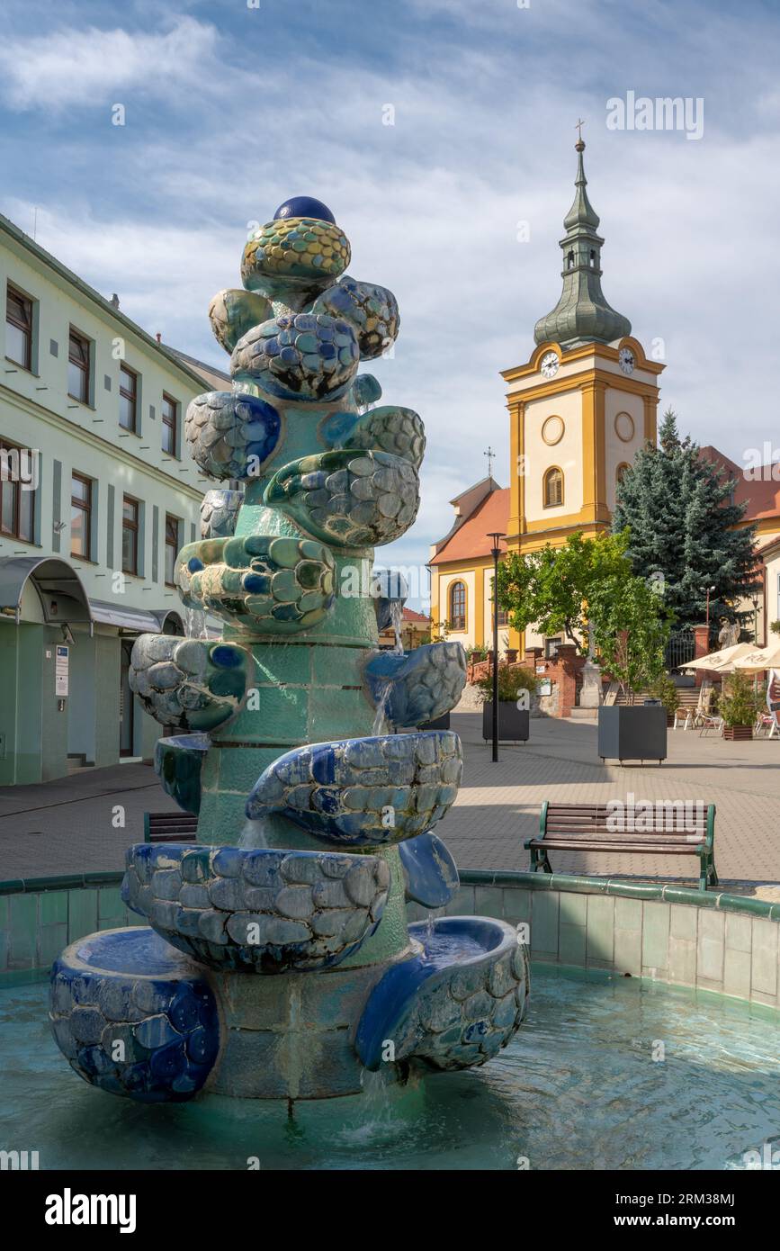 Piazza della città di Šlapanice vicino a Brno e Austerlitz, repubblica Ceca, con moderna fontana in ceramica e chiesa dell'assunzione di Maria. Foto Stock