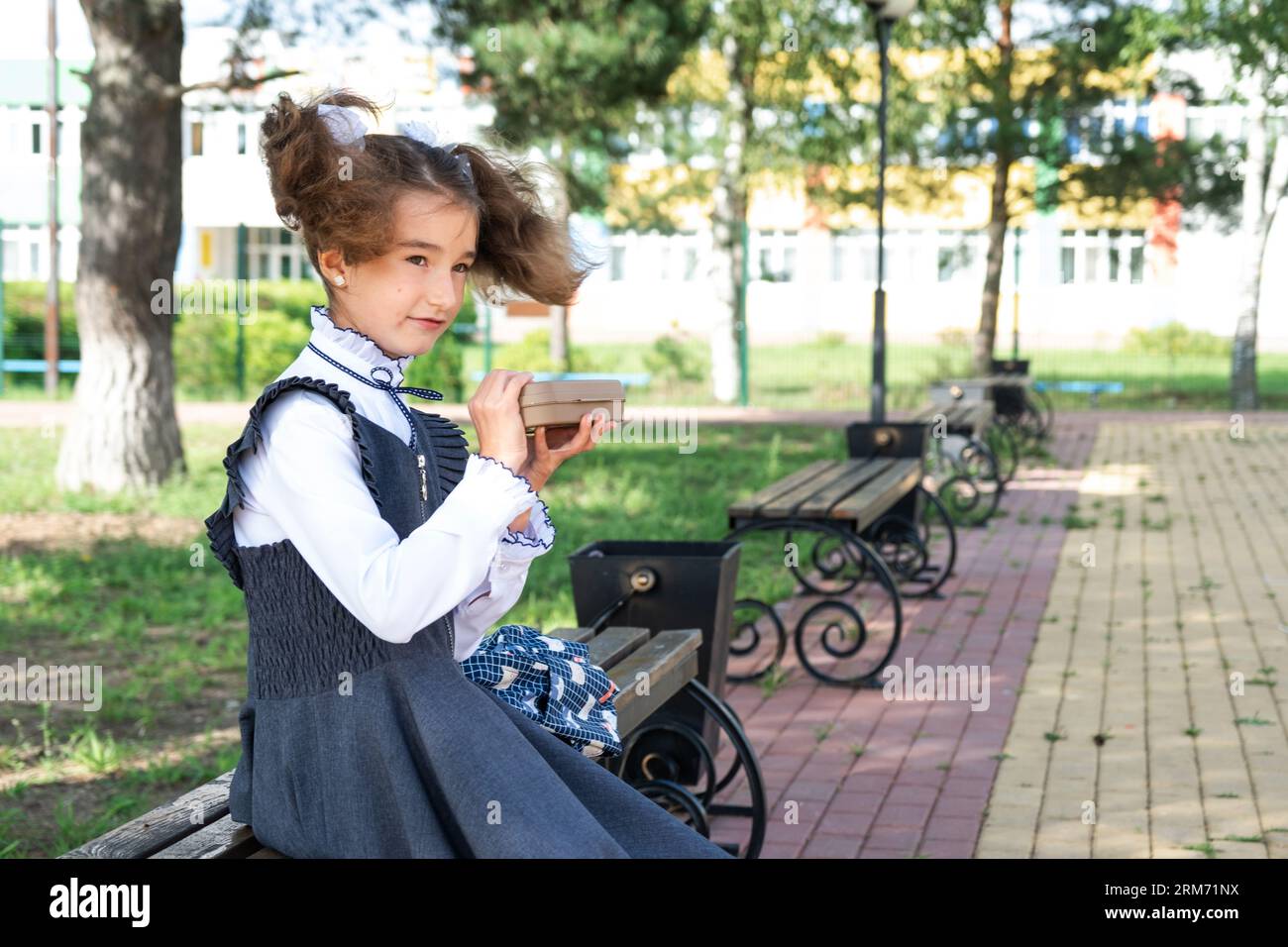 Ragazza con zaino che mangia panino confezionata in una scatola vicino a scuola. Uno spuntino veloce con un panino, cibo malsano, pranzo da scuola. Torna a scuola. Foto Stock