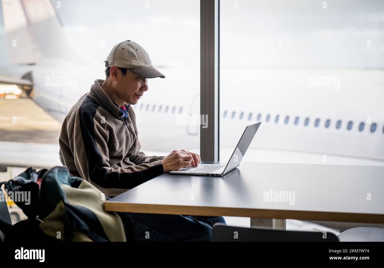 Uomo d'affari che lavora su un computer portatile all'aeroporto. Imprenditore digitale in viaggio lavora in remoto online nella sala d'imbarco di Airline hub. Foto Stock