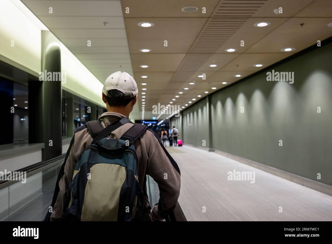 Uomo che cammina nell'area di partenza dell'aeroporto. passanti non riconoscibili in background. Foto Stock