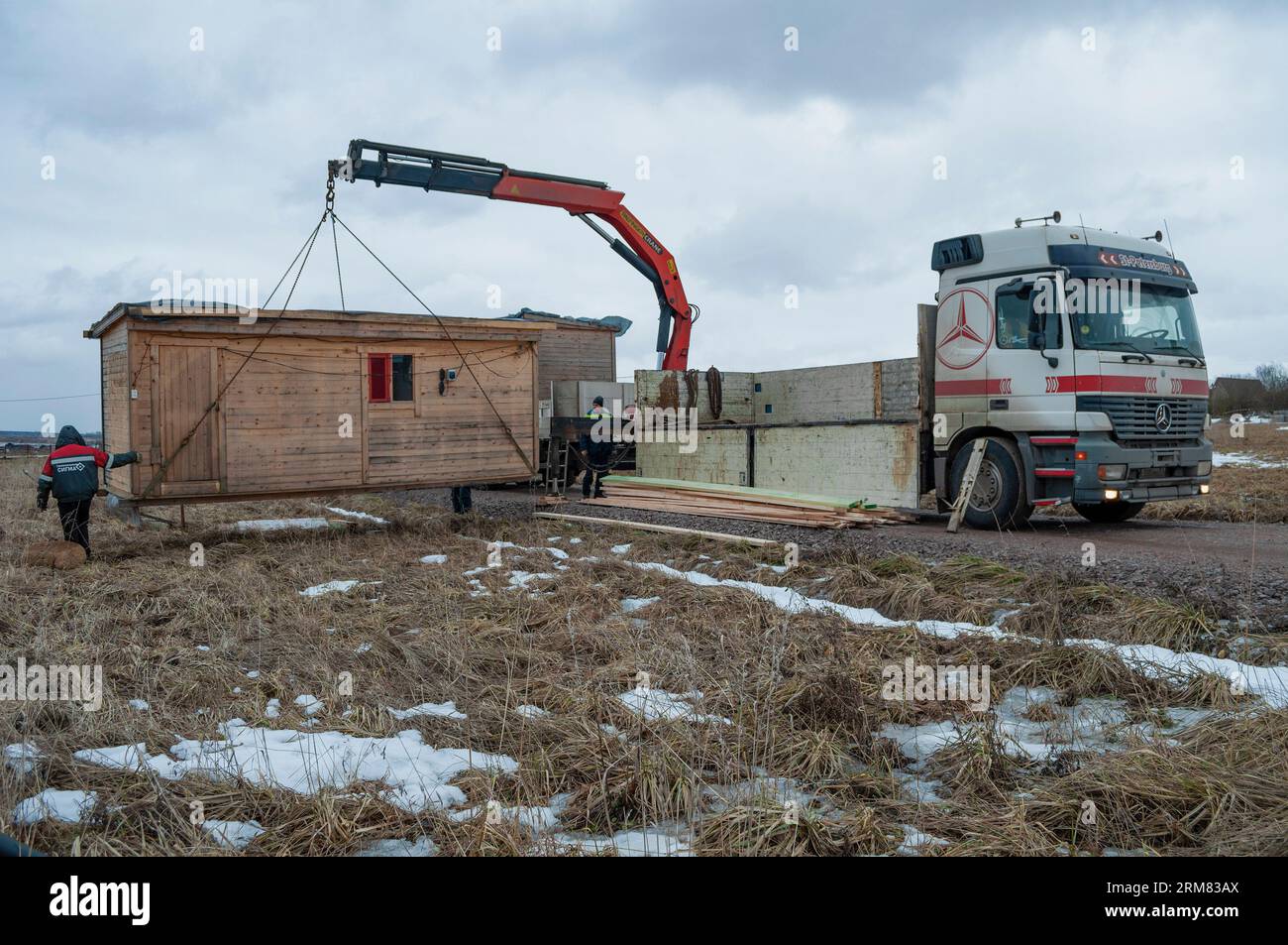 REGIONE DI LENINGRADO, RUSSIA - 4 MARZO 2021: Scarico con una gru manipolatrice di un capannone di costruzione in un sito rurale per la disposizione di un edificio Foto Stock