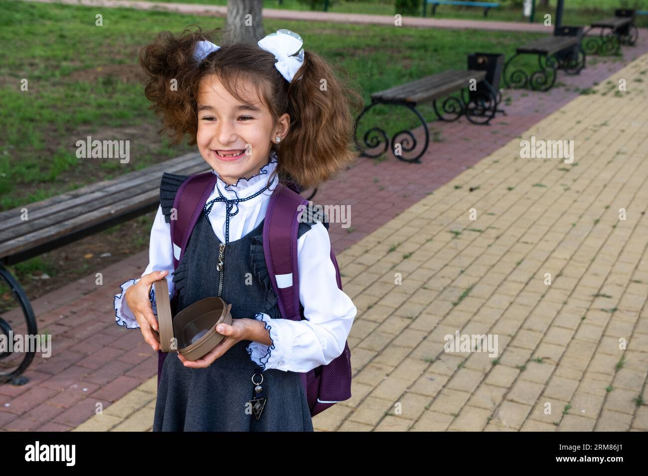 Ragazza con zaino che mangia panino confezionata in una scatola vicino a scuola. Uno spuntino veloce con un panino, cibo malsano, pranzo da scuola. Torna a scuola. Foto Stock