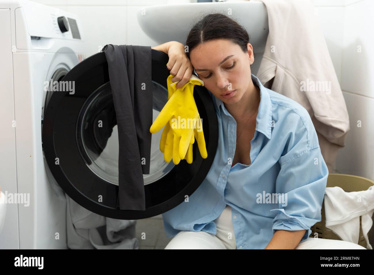 Una casalinga stanca si siede vicino alla lavanderia sporca. Routine domestica e lavoro femminile. Foto Stock