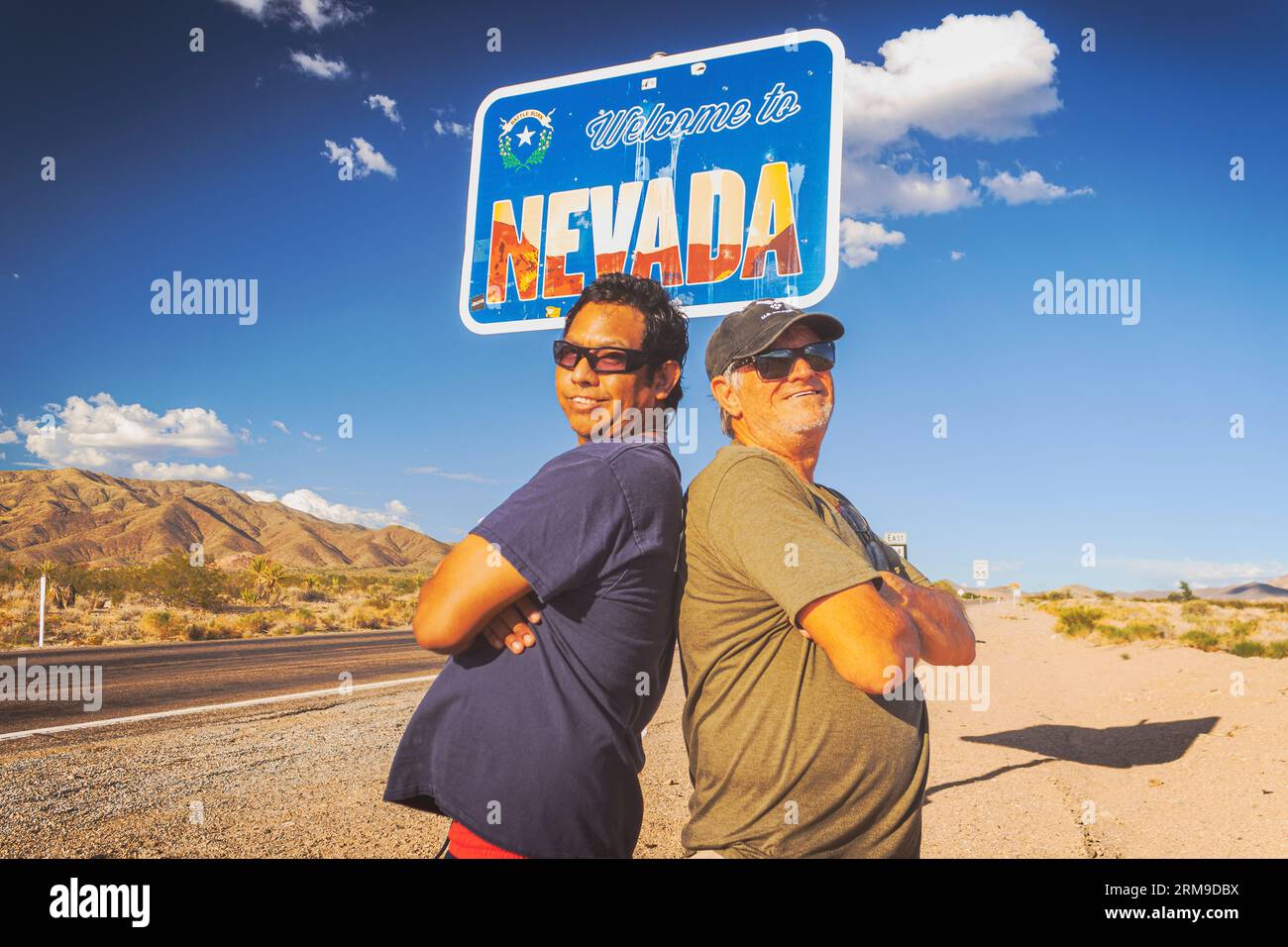 Un ritratto edificante di David e Gio Skelton, in piedi dietro e sorridendo, sotto il cartello "Welcome to Nevada" (benvenuto in Nevada) sulla California e Nevada sta Foto Stock