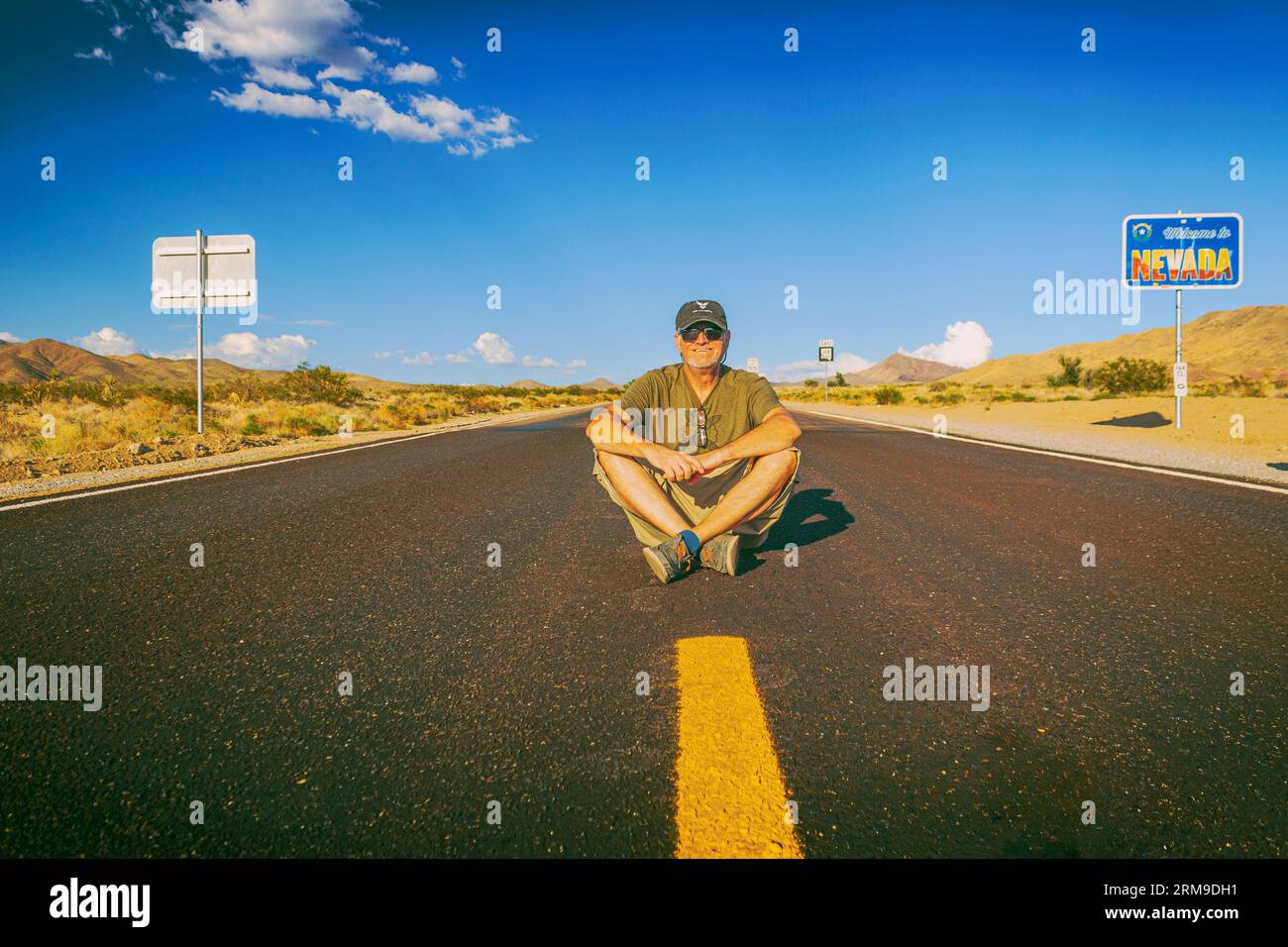 Un ritratto introspettivo di David Skelton seduto sul terreno del vuoto e raramente viaggiato Nipton Rd, che guarda nella telecamera la California e. Foto Stock