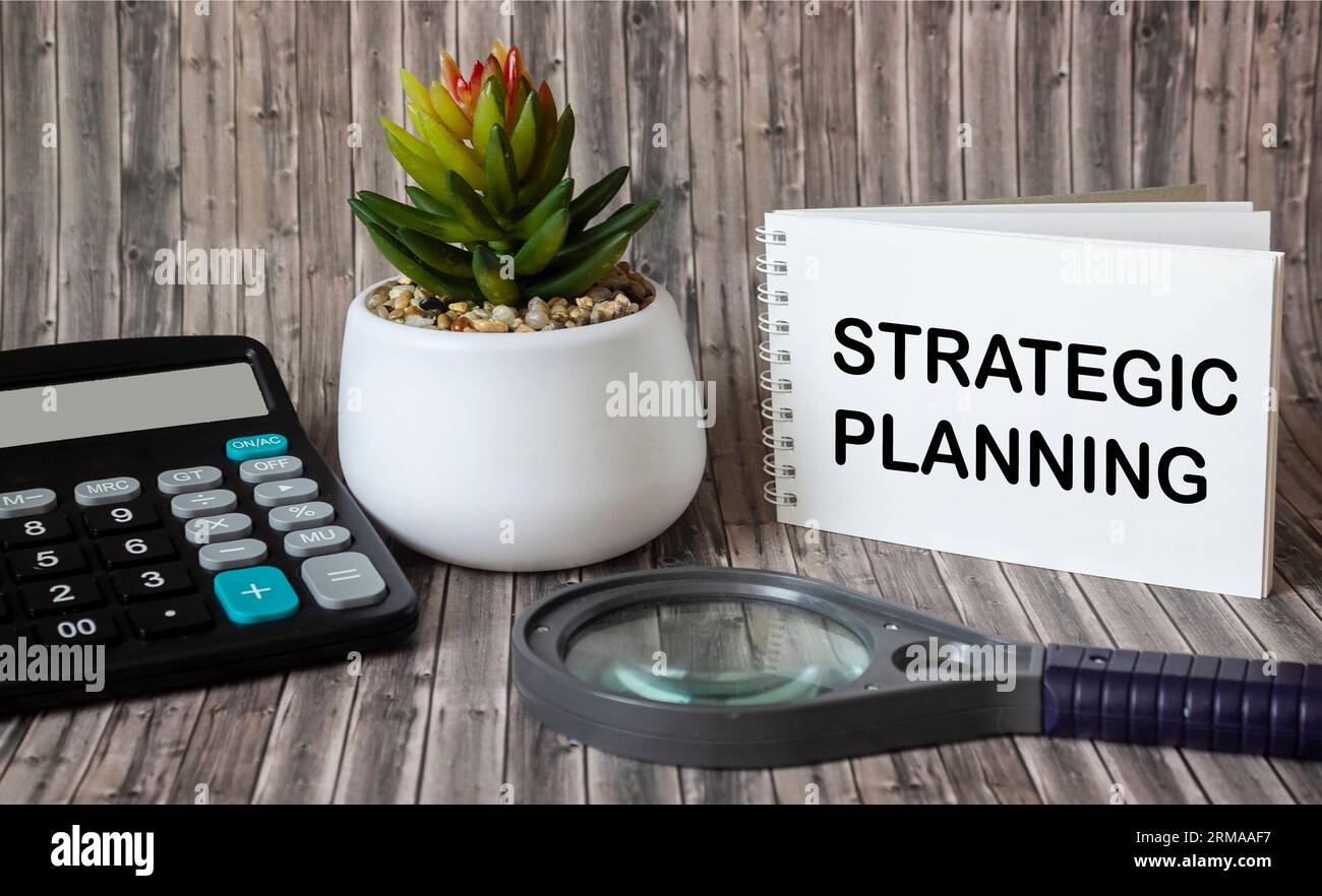 Il notebook dice pianificazione strategica. Calcolatrice con lente d'ingrandimento su sfondo di legno. Concetto economico e finanziario Foto Stock
