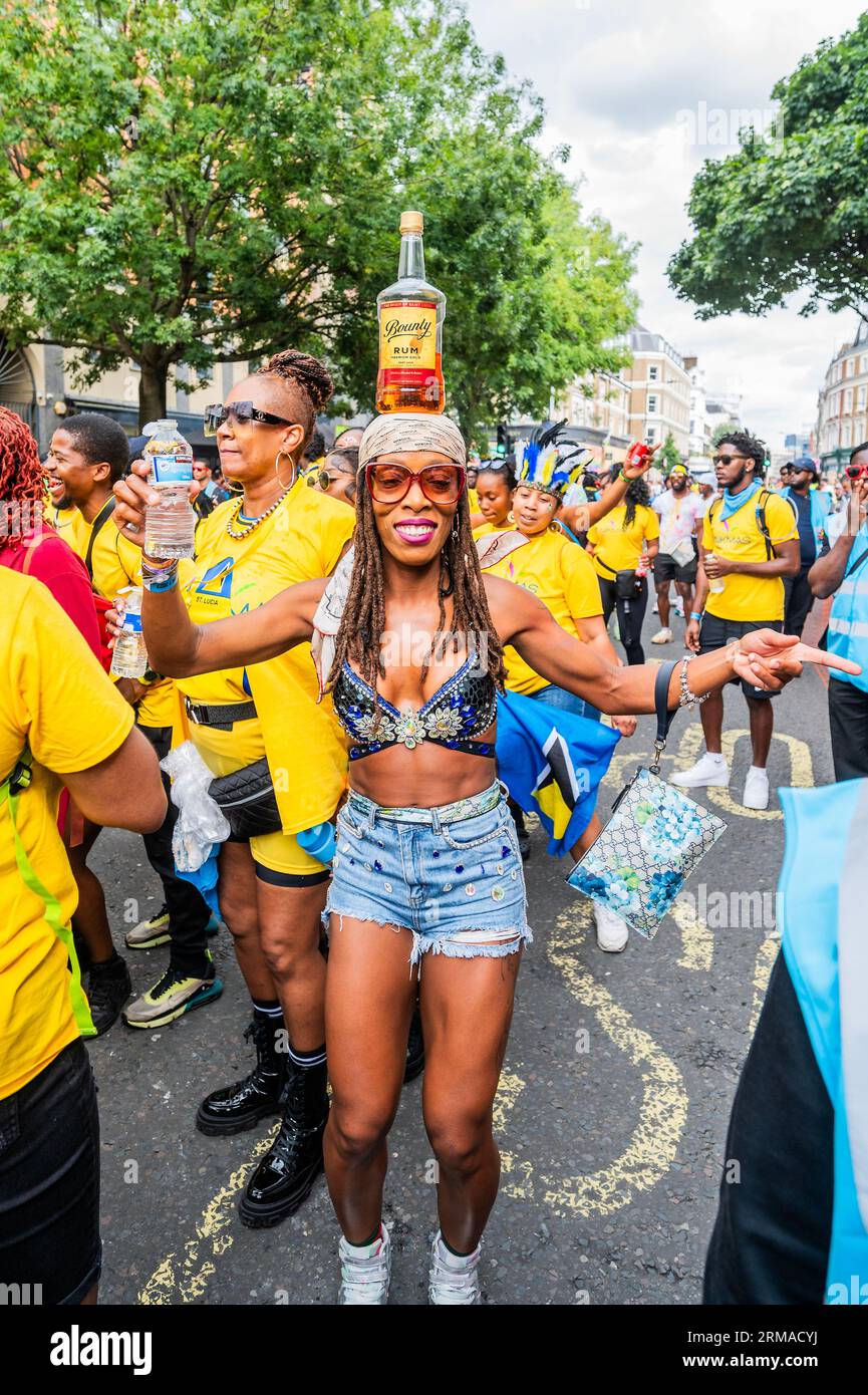 Londra, Regno Unito. 27 agosto 2023. Una donna mangia per ballare nella parata con una grande bottiglia di rum bilanciata sulla testa - la domenica del Carnevale di Notting Hill, tradizionalmente giorno dei bambini. L'evento annuale per le strade del Royal Borough di Kensington e Chelsea, durante il fine settimana festivo di agosto. È guidato da membri della comunità britannica delle Indie occidentali e attrae circa un milione di persone all'anno, rendendolo uno dei più grandi festival di strada del mondo. Crediti: Guy Bell/Alamy Live News Foto Stock