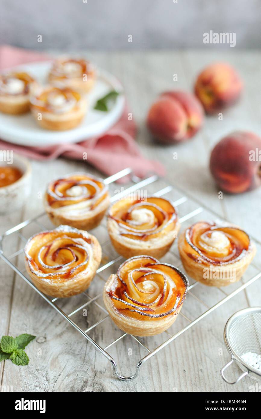 Rose di nettarina fatte di pasta sfoglia, su un piatto bianco. Involtini di pasta sfoglia burrosi, friabili e croccanti con strati di saporite fette di nettarina. Pisolino rosa Foto Stock