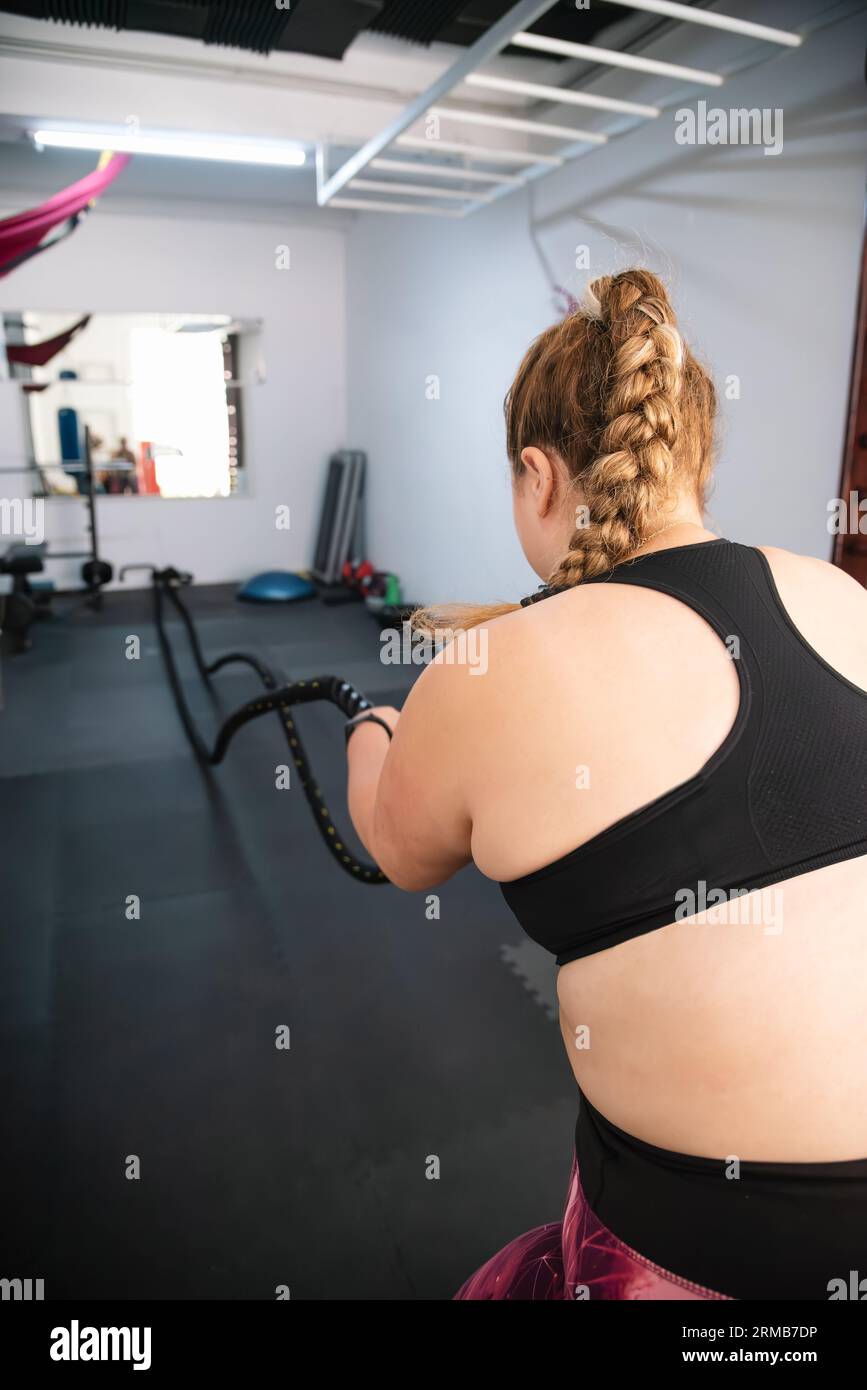 Una giovane donna, piena di dedizione, si impegna in un'intensa sessione di allenamento con corde di battaglia nell'ambiente dinamico di una palestra ben attrezzata Foto Stock