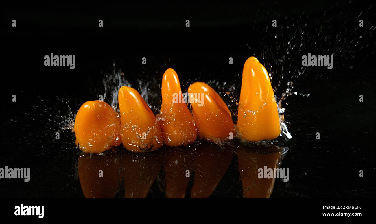 Peperoni dolci gialli, capsicum annuum, verdure che cadono sull'acqua su fondo nero, Foto Stock