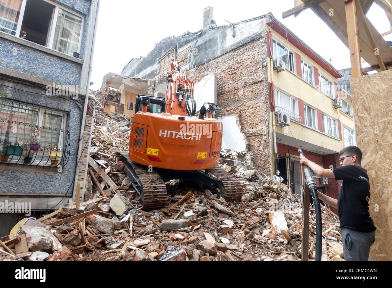 Hitachi Construction Excavator demolisce un edificio in una strada stretta a Sisli Istanbul Turchia. Un giovane che annaffiava Foto Stock