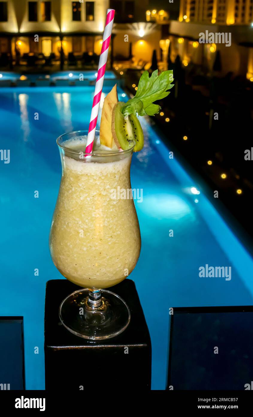 Bicchiere di cocktail Pina colada con paglia contro una piscina laguna blu. Bicchiere di Kiwi Colada sullo sfondo della piscina notturna, l'hotel Amman Sheraton Jordan Foto Stock