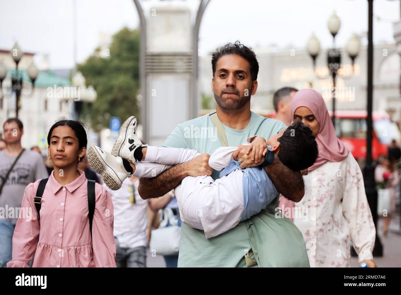 Famiglia araba che cammina lungo la strada della città. L'uomo porta un bambino in braccio Foto Stock