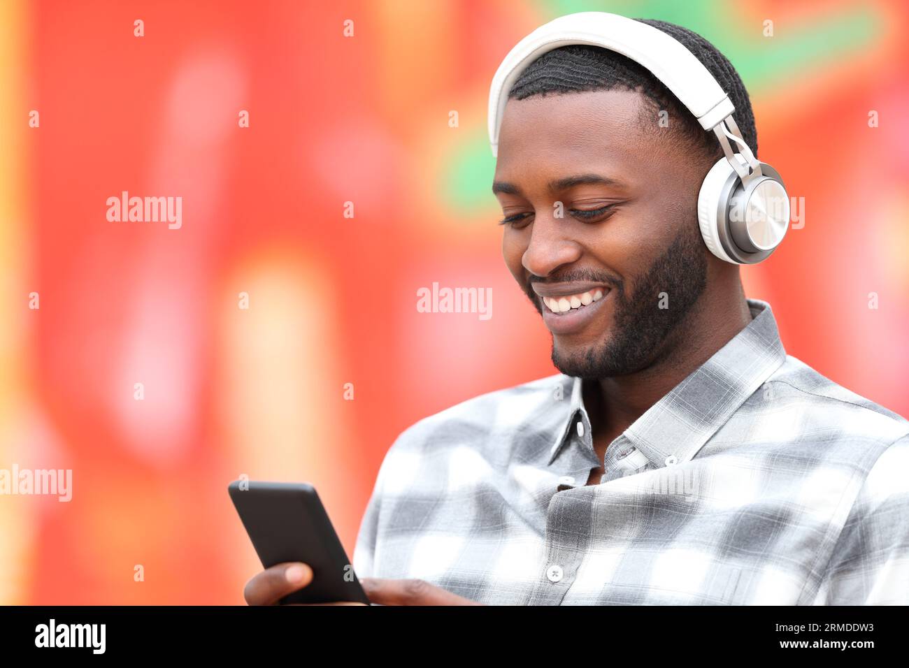 L'uomo nero felice ascolta la musica con le cuffie e il telefono su sfondo rosso Foto Stock