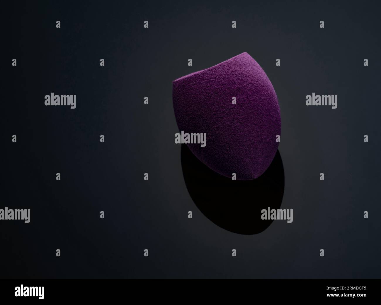 Spugna per il trucco viola su sfondo scuro. Spugna cosmetica morbida per il trucco. Spugna per il trucco a estremità piatta. Frullatore di bellezza per un trucco impeccabile. Strumento per il trucco. Foto Stock