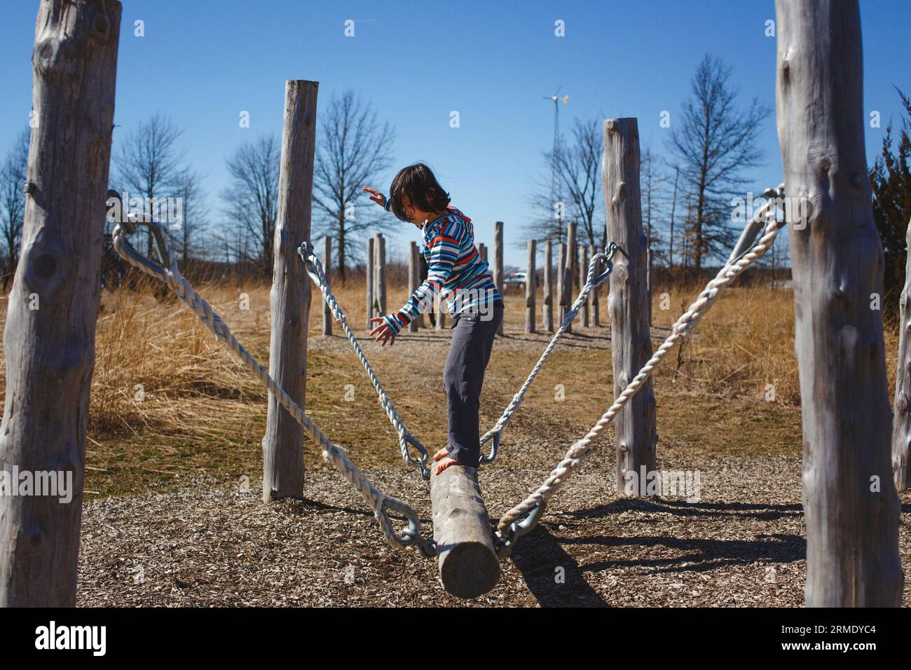 vista laterale di un bambino a piedi nudi in equilibrio su un percorso ad ostacoli di tronco Foto Stock
