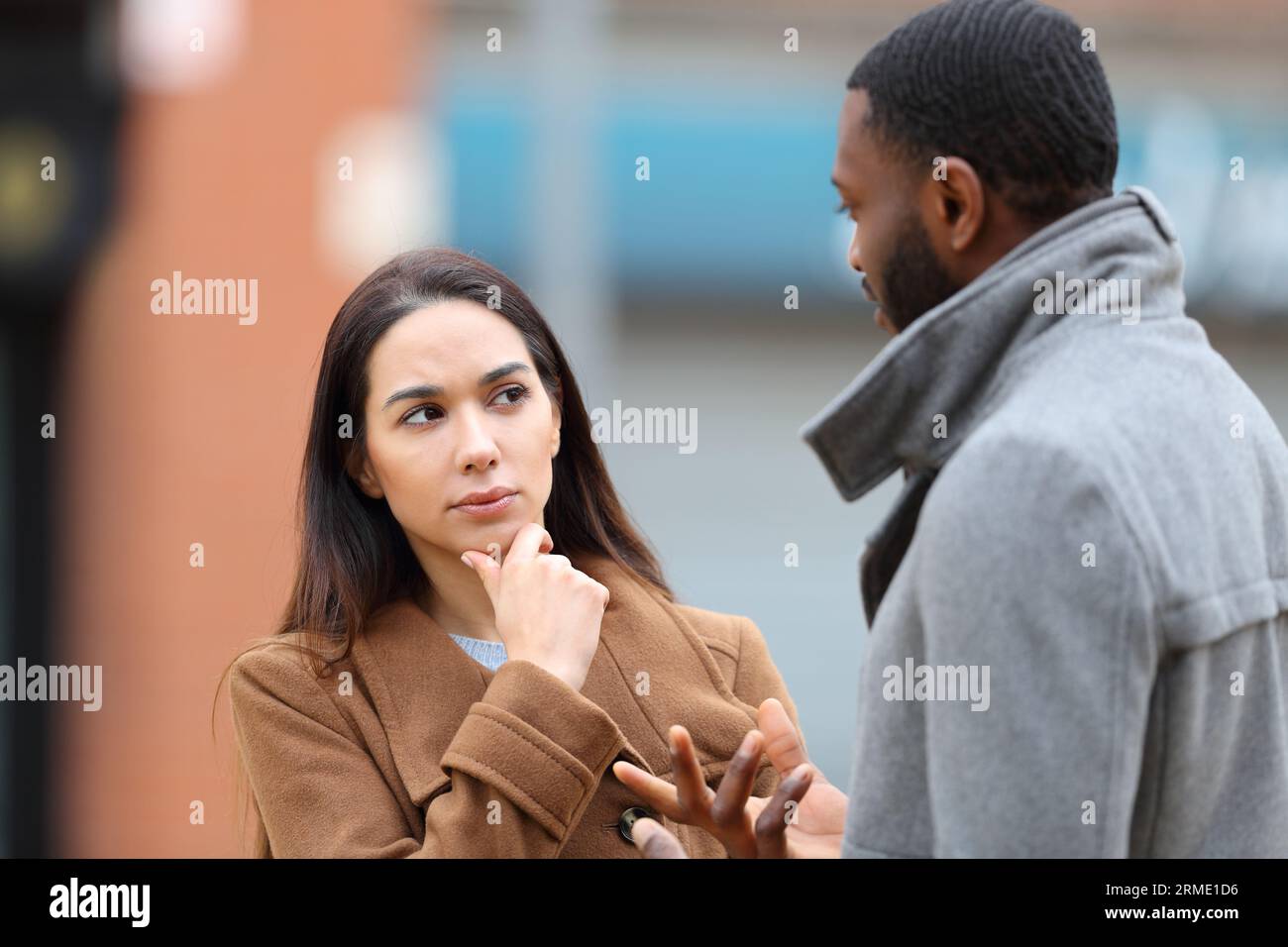 Donna dubbiosa che ascolta un uomo che parla per strada in inverno Foto Stock