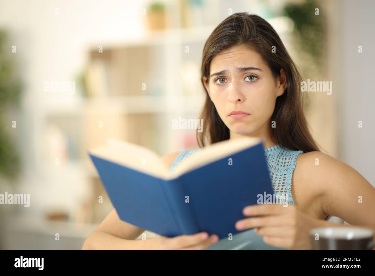 Triste lettore di libri che guarda la fotocamera seduto a casa Foto Stock