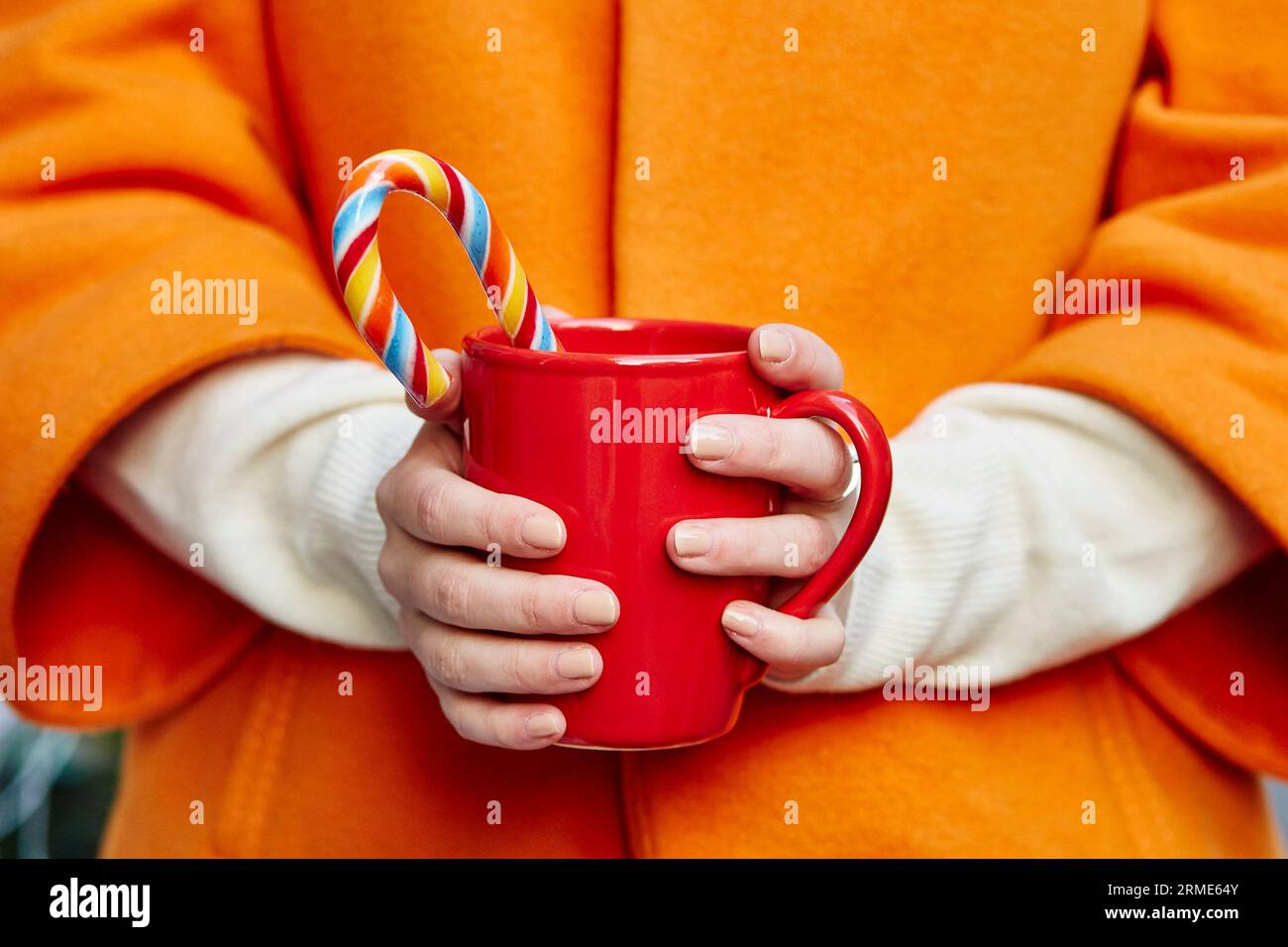 Le mani di una donna in guanti di lana reggono un'accogliente tazza con cioccolata calda, tè o caffè e una canna di caramelle natalizie Foto Stock