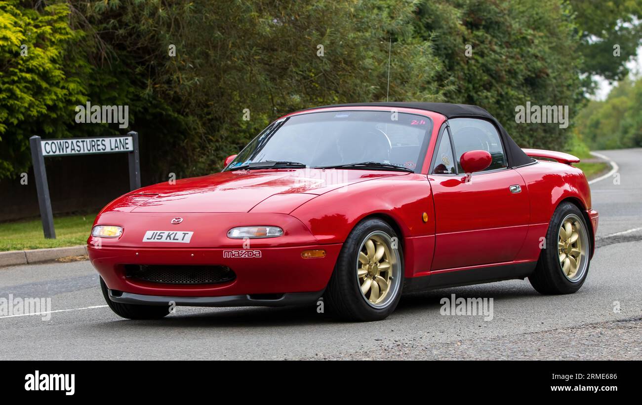 Whittlebury, Northants, Regno Unito - 26 agosto 2023:1991 auto sportiva Mazda MX 5 rossa che viaggia su una strada di campagna inglese Foto Stock