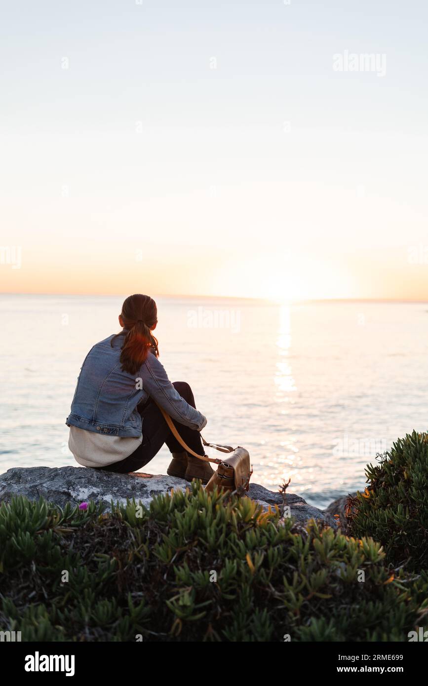 Una donna che guarda un tramonto su una costa rocciosa dell'oceano Foto Stock