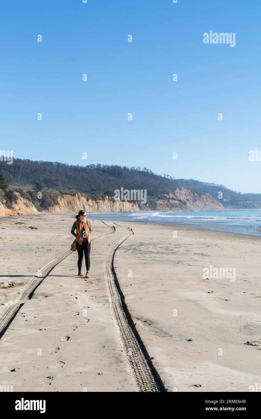 Una donna che cammina su una spiaggia con le tracce di pneumatici in California Foto Stock