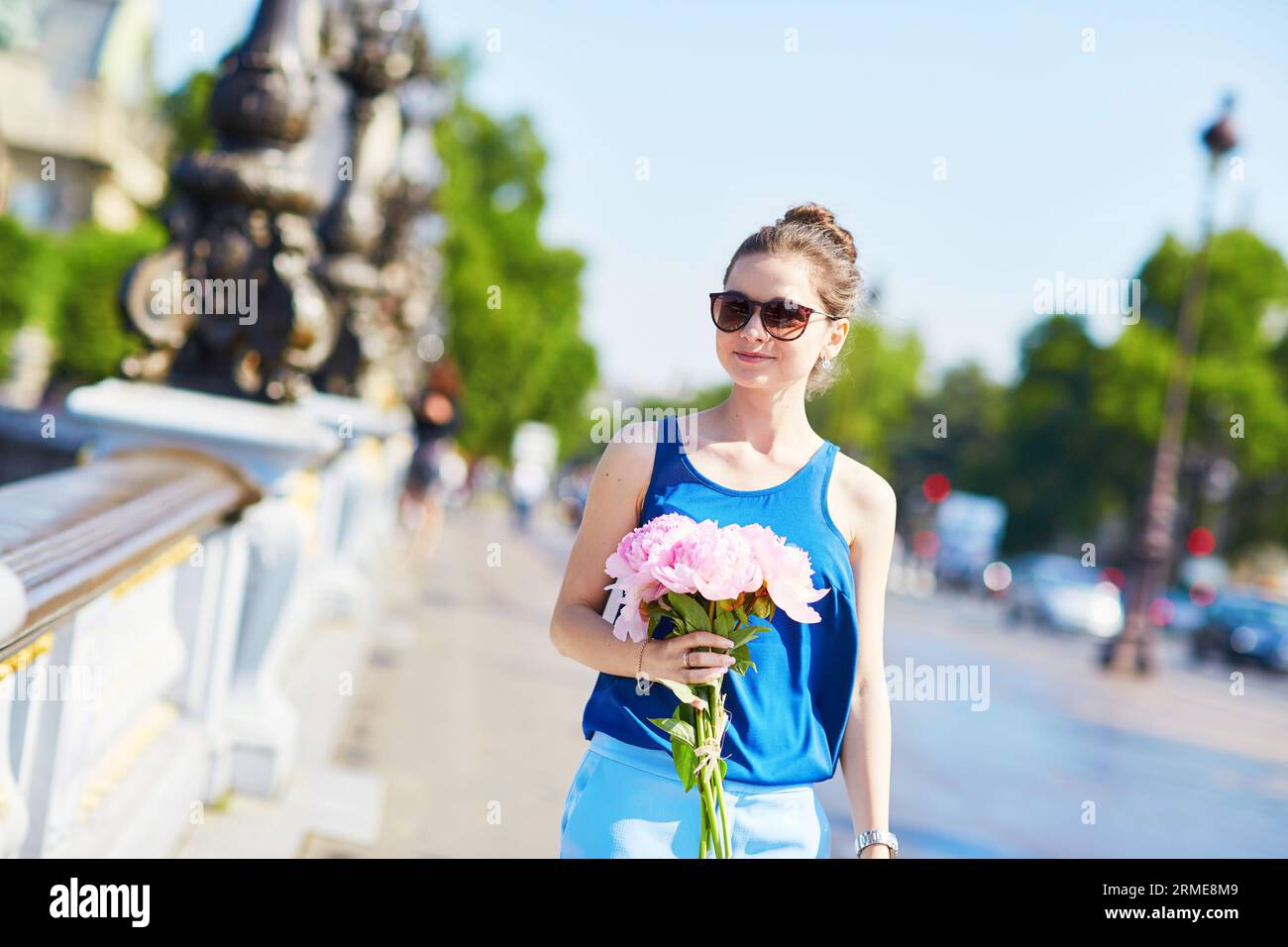 Bella giovane donna parigina in camicetta blu con un mazzo di peonie rosa sul Pont Alexandre III a Parigi, in Francia Foto Stock