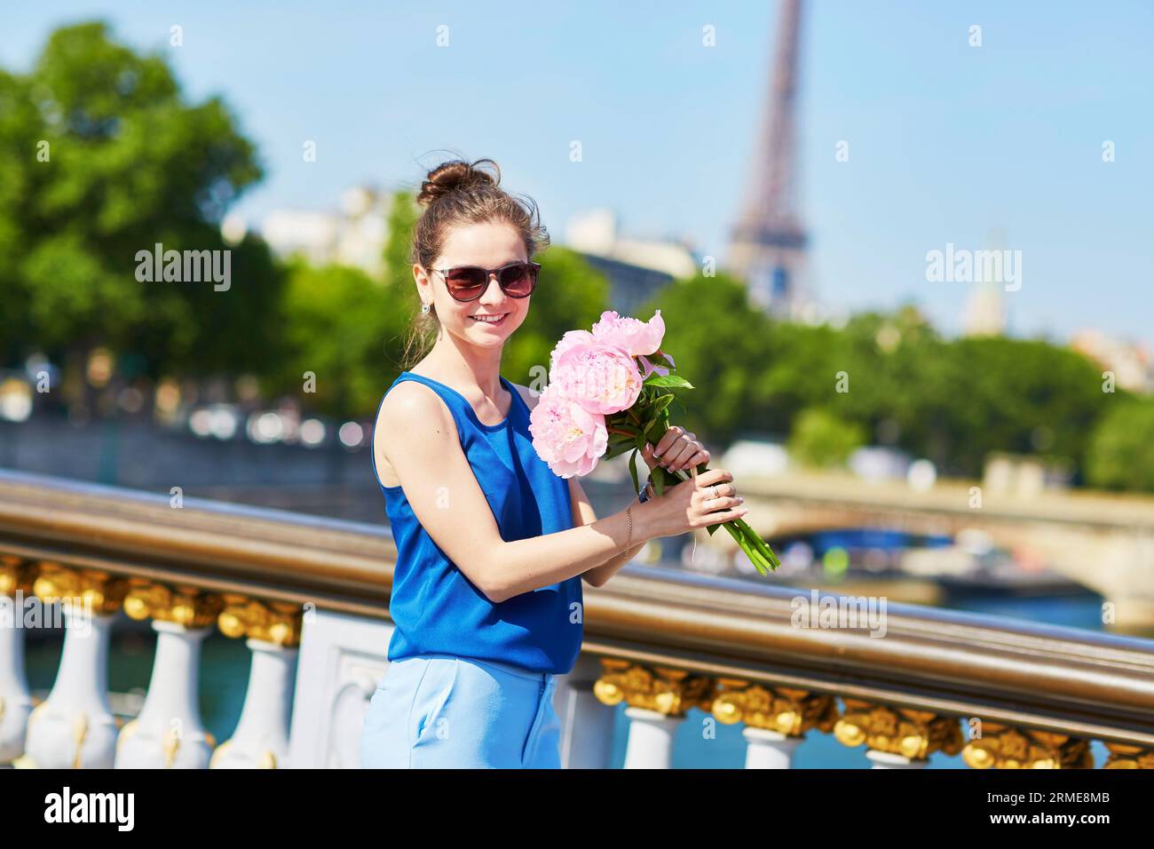 Bella giovane donna parigina in camicetta blu con un mazzo di peonie rosa sul Pont Alexandre III a Parigi, in Francia Foto Stock