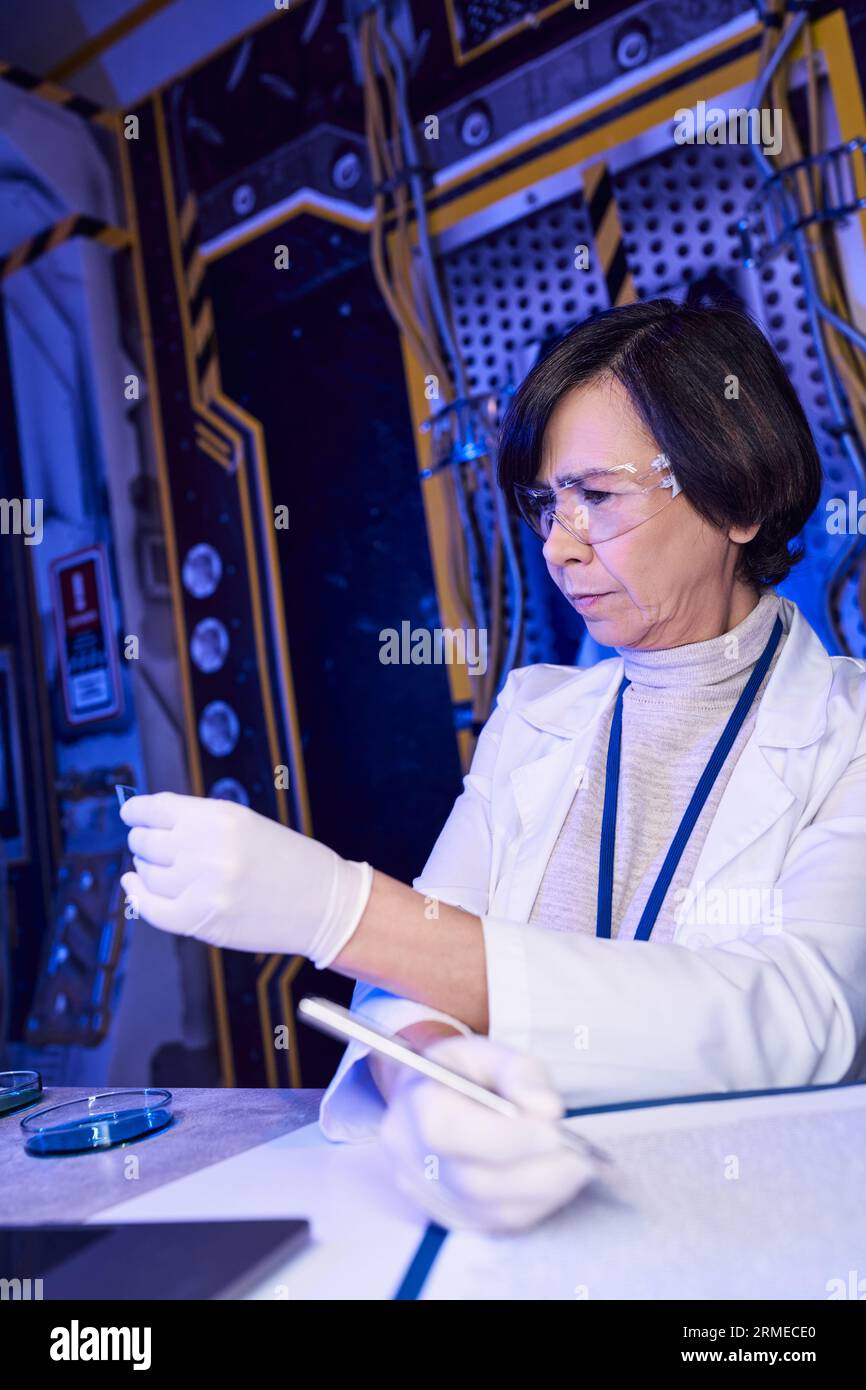 donna scienziata con occhiali che guarda la carta del tornasole, esplora la vita aliena in un laboratorio innovativo Foto Stock