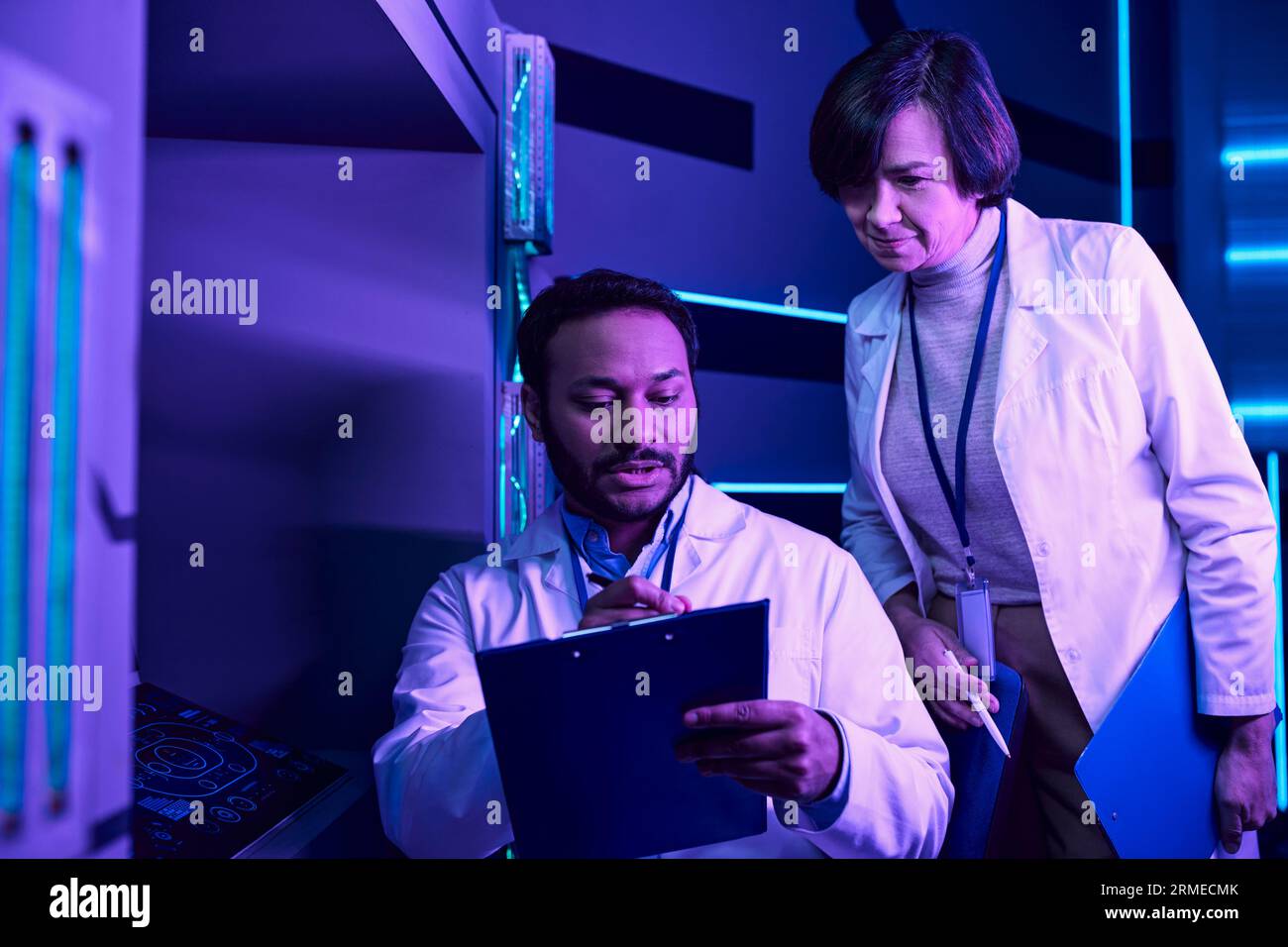 Scienziati indù maschi e adulti femmine analizzano i dati nel Neon-Lit Science Center Foto Stock