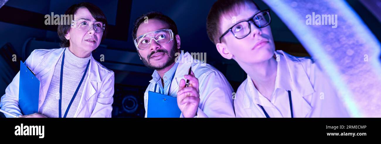 Banner, Futuristic Exploration: Diverse-Age Scientists Investigate Device nel Neon-Lit Science Center Foto Stock