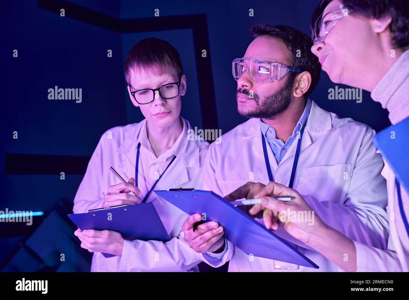 Collaborazione futuristica: Scienziati multigenerazionali lavorano insieme nel Neon-Lit Science Center Foto Stock