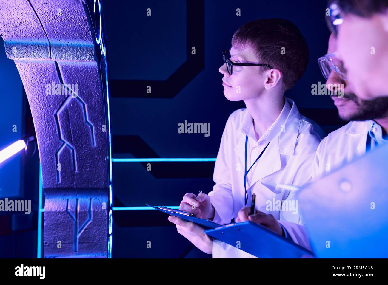 Osservazioni futuristiche: Scienziati di età varia esaminano il dispositivo nel Neon-Lit Science Center Foto Stock