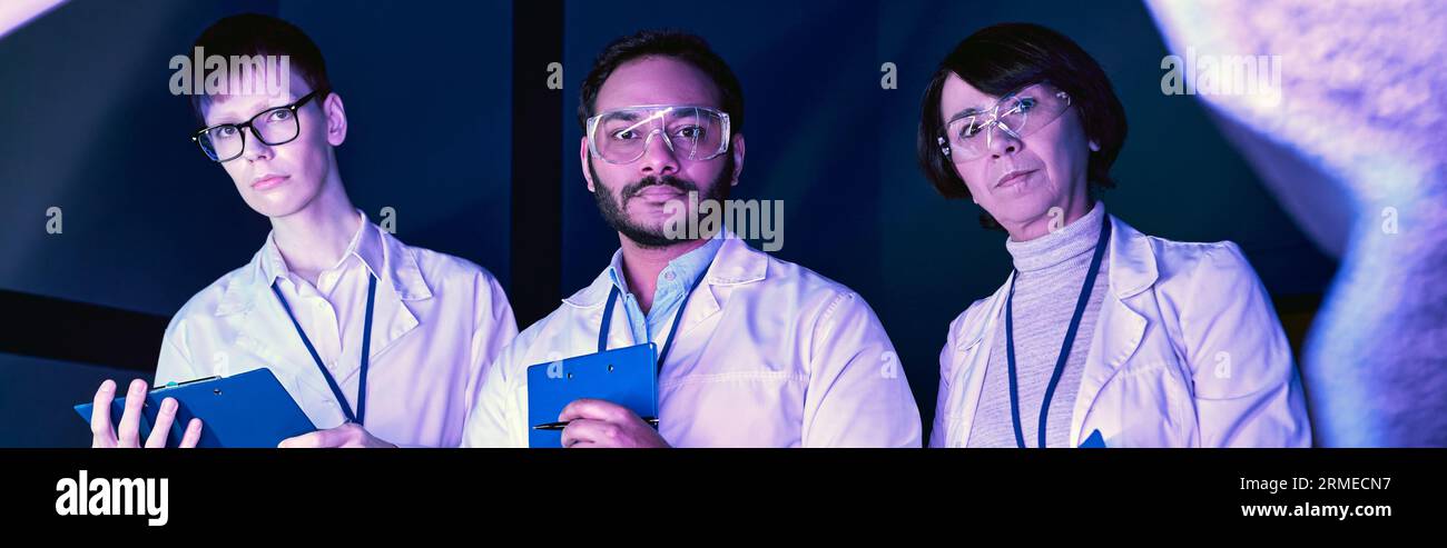 Banner, tre scienziati esaminano il dispositivo appena creato nel Neon-Lit Science Center Foto Stock