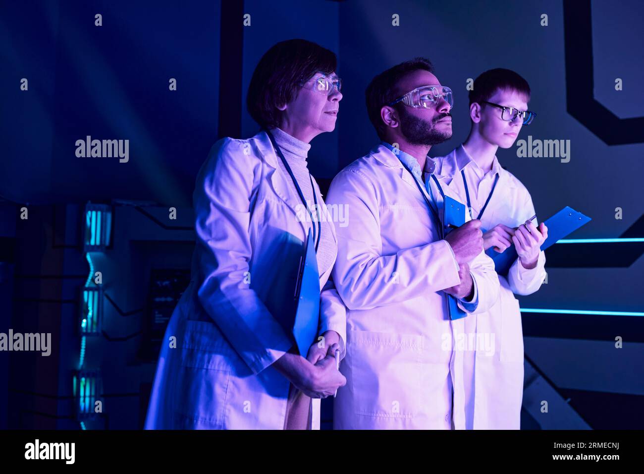 Osservazione futuristica: Tre scienziati esaminano il dispositivo appena creato nel Neon-Lit Science Center Foto Stock