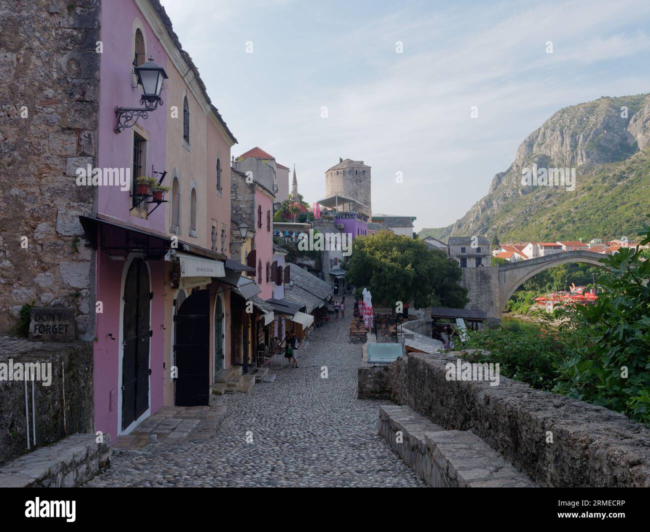 Strada acciottolata della città vecchia, sito UNESCO nella città di Mostar con Stari Most (Ponte Vecchio) e montagne a destra, Bosnia ed Erzegovina, 28 agosto 2023. Foto Stock