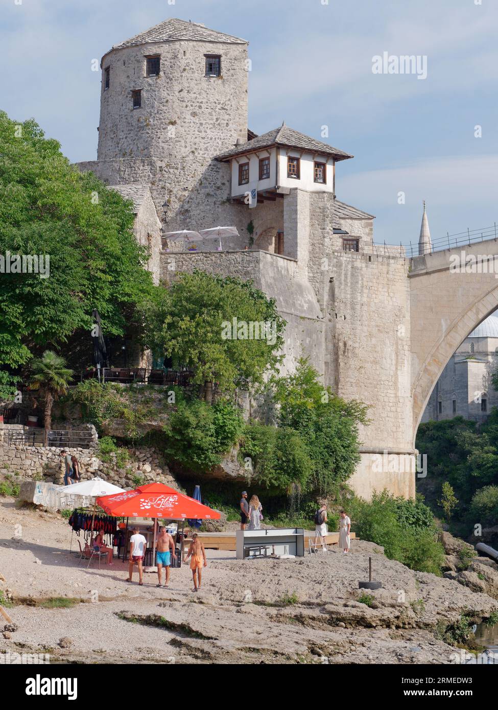 Parte di Stari Most (Ponte Vecchio) e Torre sul fiume Neretva con turisti sulle rocce sottostanti. Mostar, Bosnia ed Erzegovina, 26 agosto 2023. Foto Stock