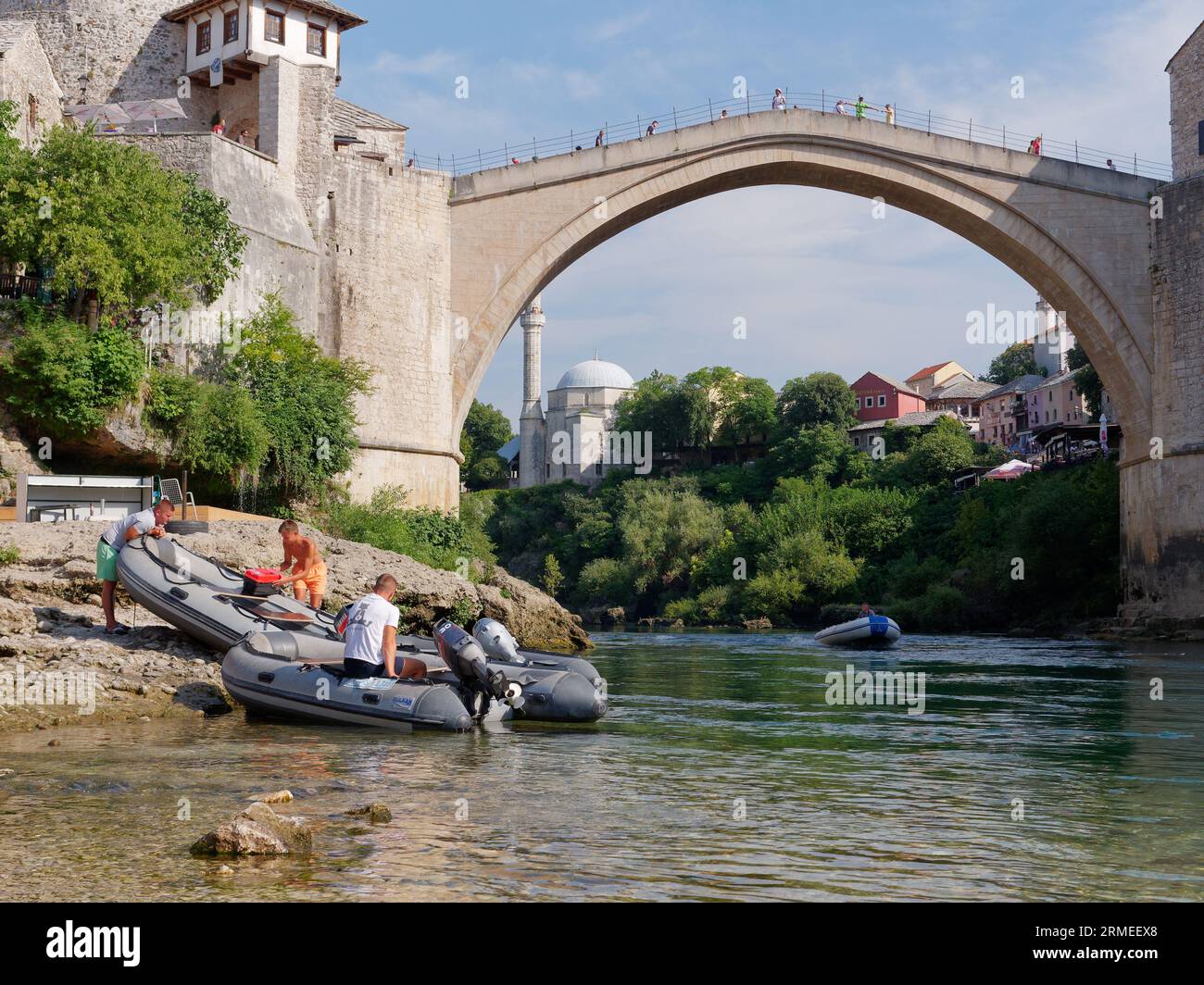 Stari Most (Ponte Vecchio) con barche sulla spiaggia lungo il fiume Neretva con barche. Città di Mostar, Bosnia ed Erzegovina, 26 agosto 2023. Foto Stock