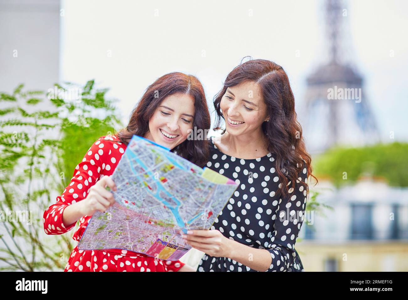 Bellissime sorelle gemelle che usano la mappa di fronte alla Torre Eiffel durante il viaggio a Parigi, in Francia. Le felici ragazze sorridenti si godono le loro vacanze in Europa Foto Stock