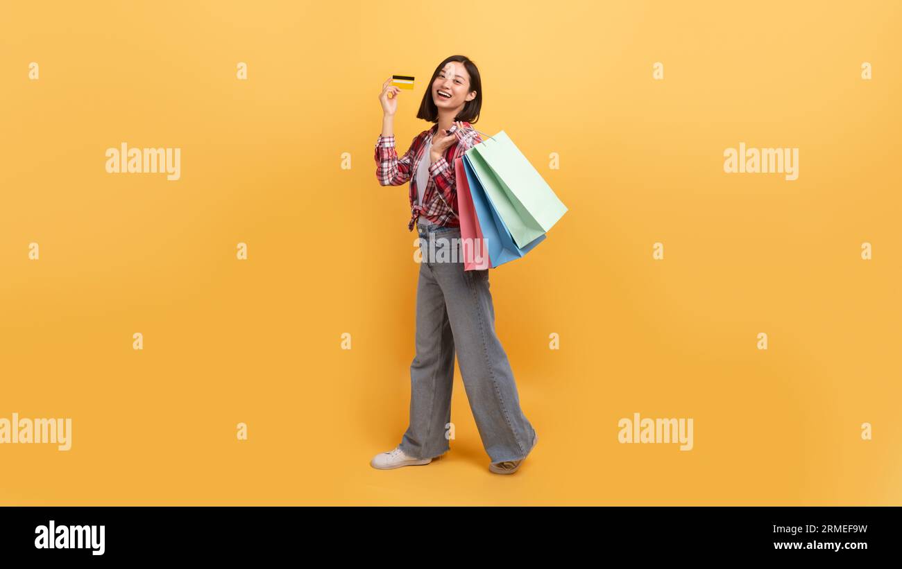 Concetto di shopping illimitato. Signora asiatica che tiene borse colorate per gli acquirenti e mostra carta di credito, lunghezza intera, spazio fotocopie Foto Stock